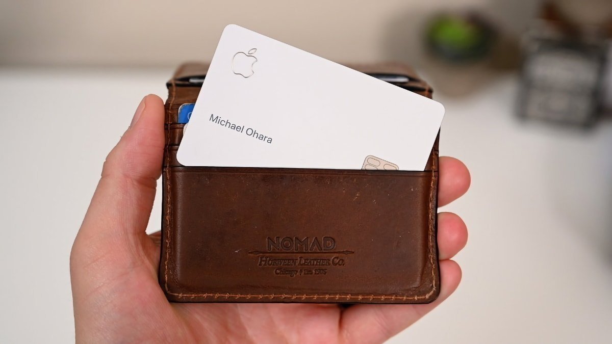 A hand holding a brown leather wallet with a white card featuring an Apple logo partially inserted into it.