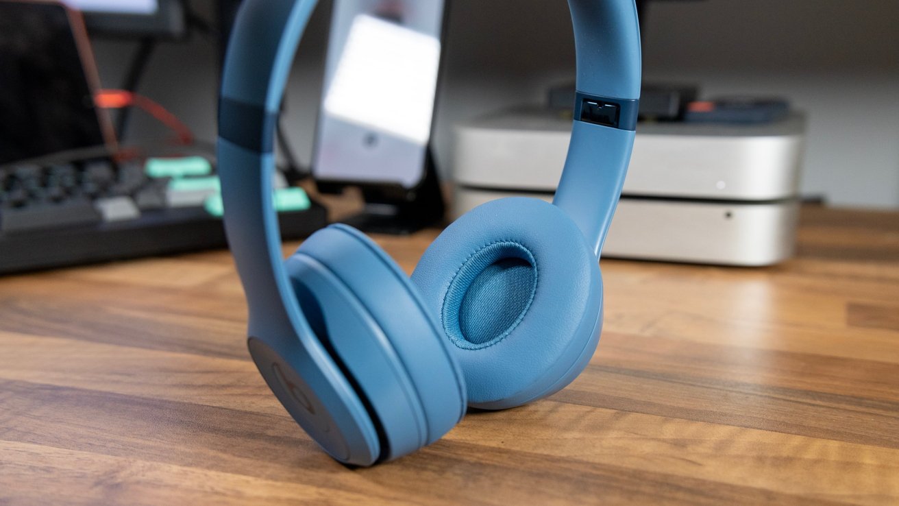 Blue over-ear Beats Solo 4 headphones on a wooden desk.