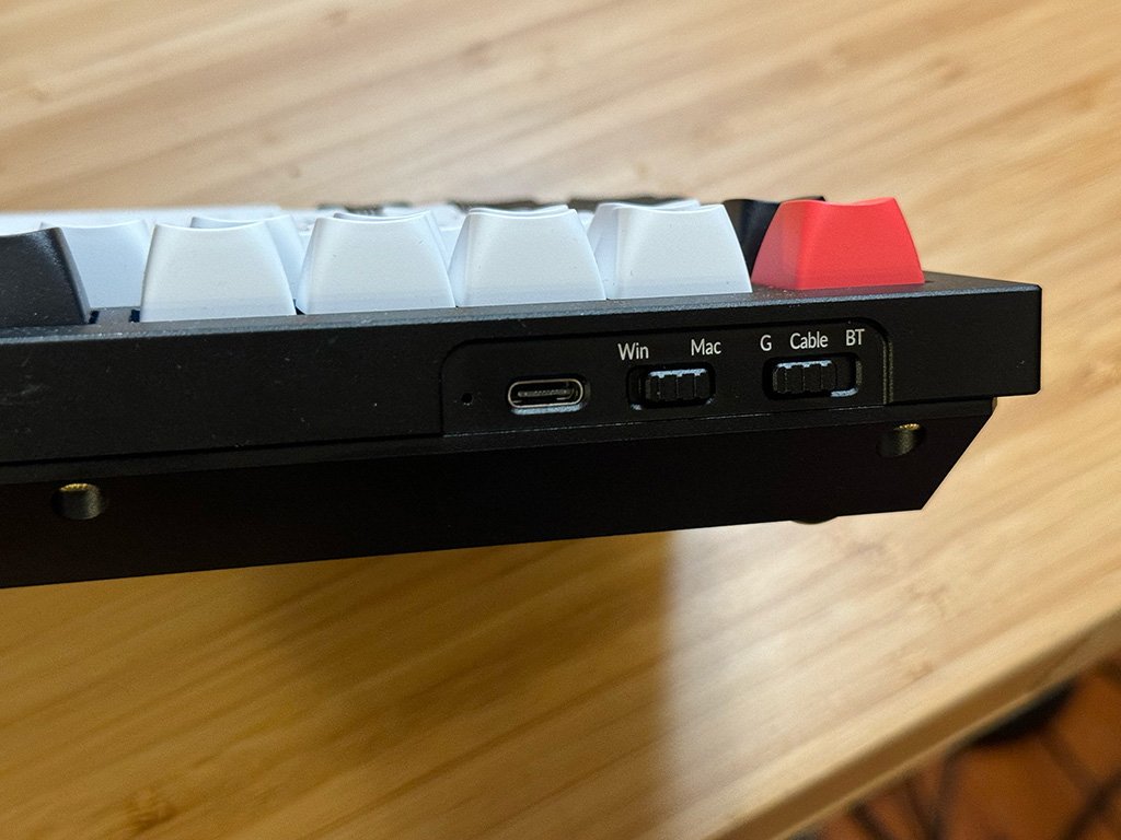 Close-up of a keyboard's edge with selector switches for Win/Mac and connection types, and a USB-C port visible.