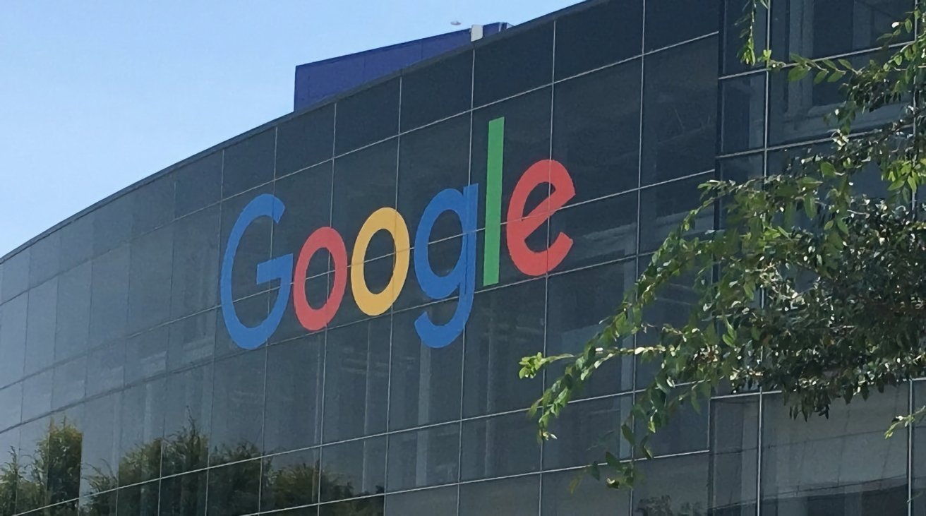 Google logo on the exterior of a modern building with reflective glass windows, surrounded by foliage under a clear sky.