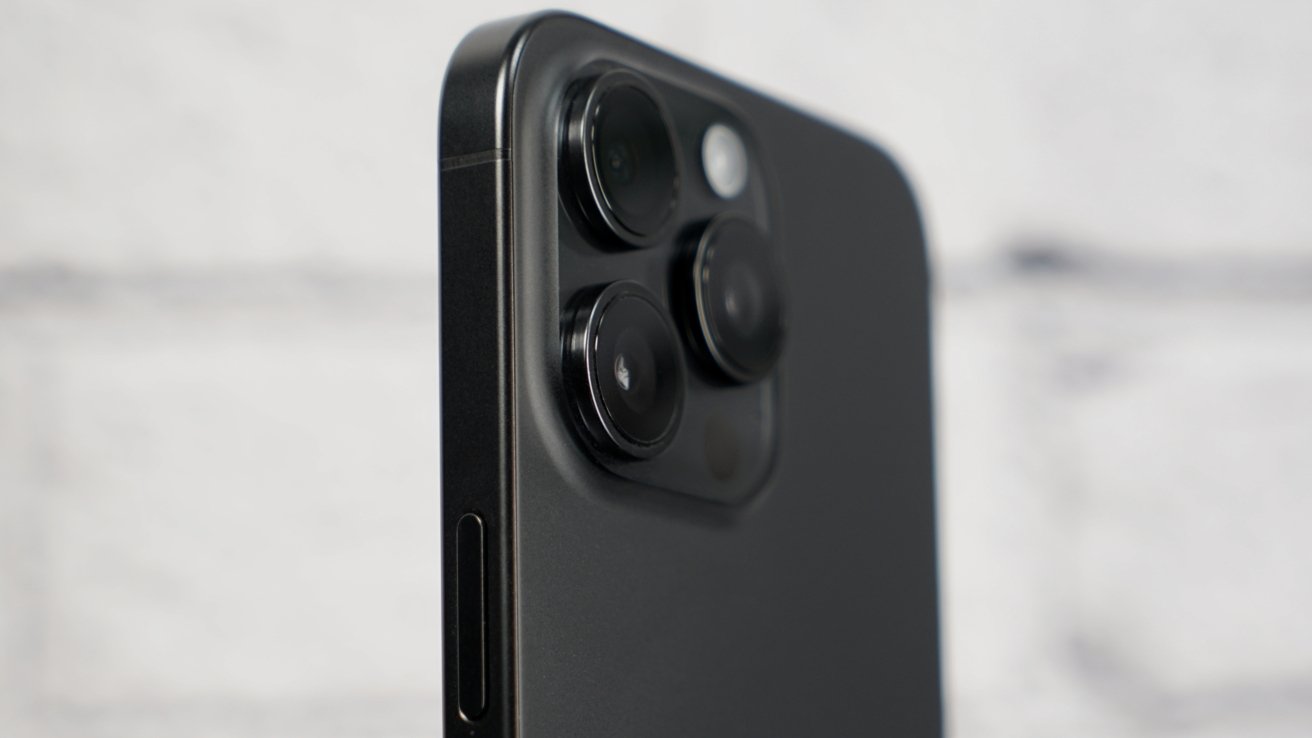 The back of an iPhone 15 Pro Max against a white brick background