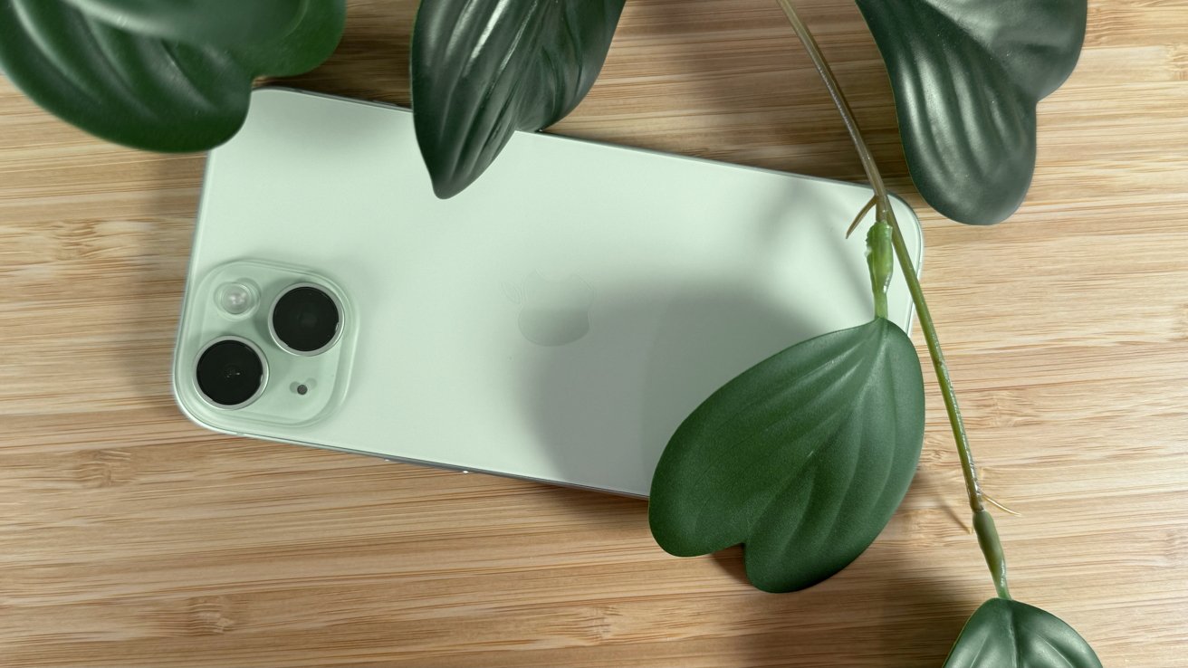 A green iPhone 15 on a desk with artificial leaves visible
