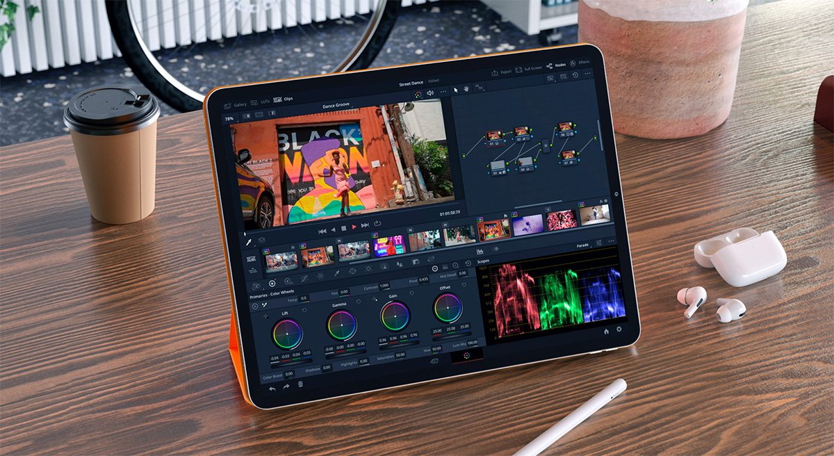Tablet displaying Resolve video editing software for iPad with colorful graphs and clips on a wooden desk, beside a coffee cup, earphones, and a stylus.