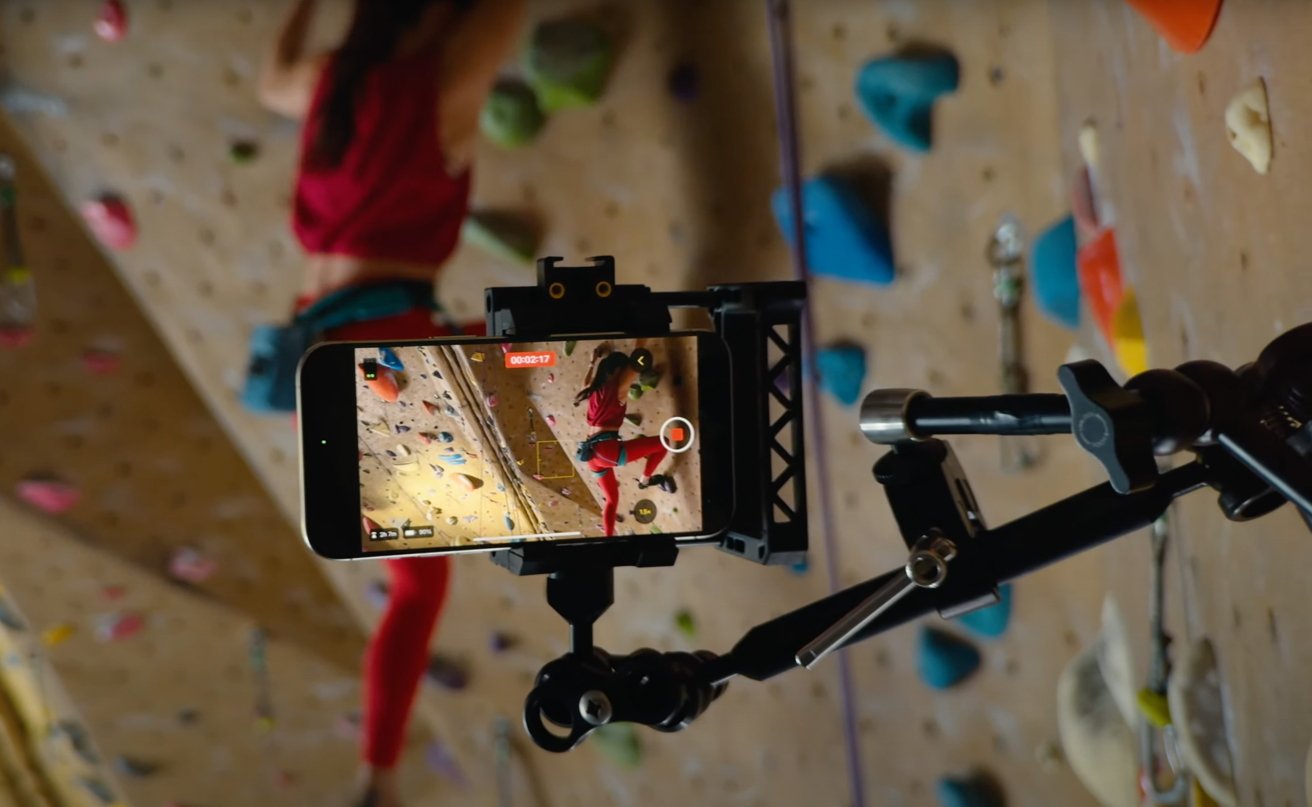 iPhone on tripod capturing a climber ascending an indoor rock wall, displayed on screen, with colorful holds in blurred background.