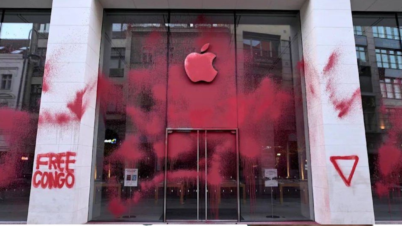 A storefront with a large apple logo splattered with red paint and 'FREE CONGO' written on the side column.