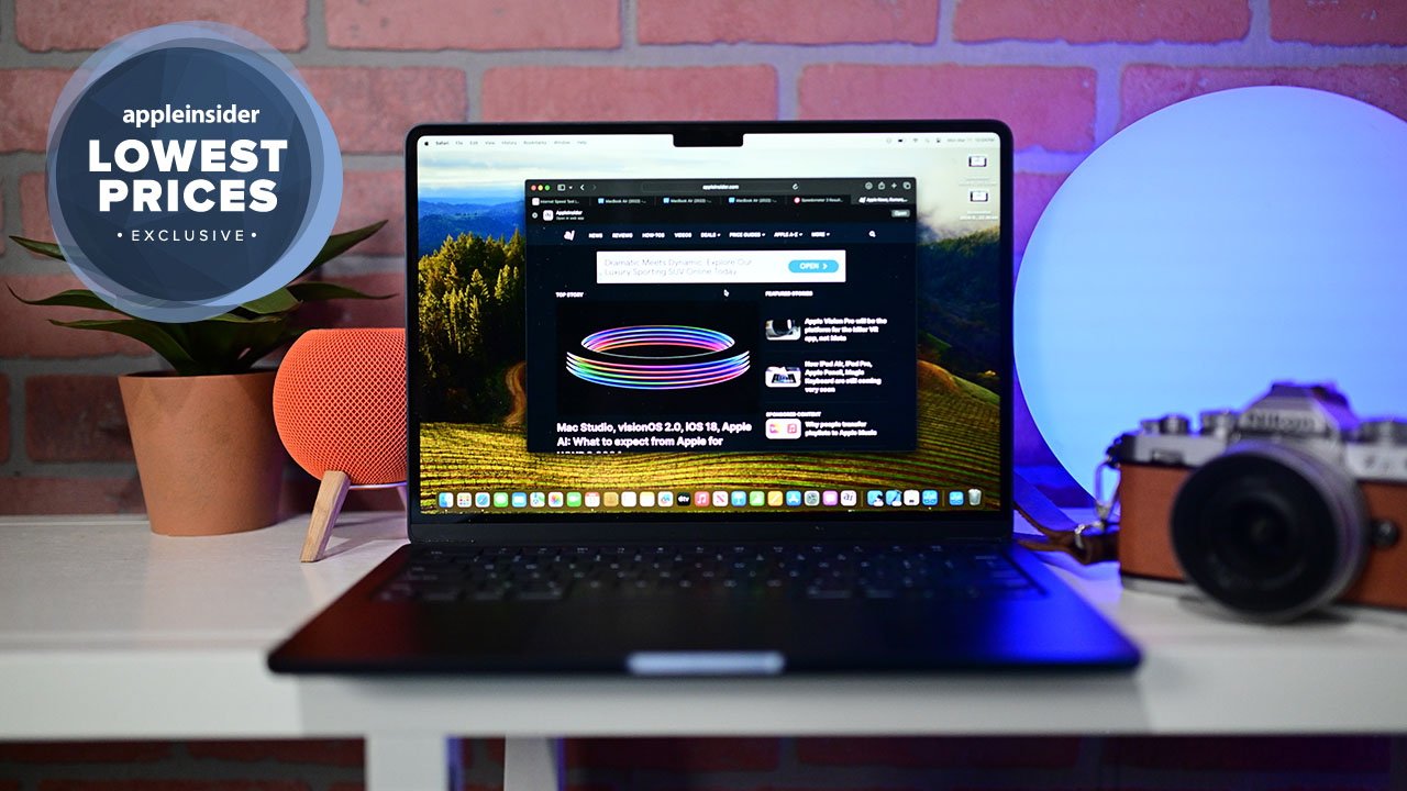 Apple's latest MacBook Air laptop on a desk displaying AppleInsider website, flanked by a HomePod speaker, a potted plant, and a vintage Nikon camera, with a lit circular lamp in the background.