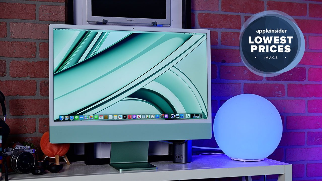 A Green 24-inch iMac on a desk with a brick wall background, a blue globe light, and a 'Lowest Prices' sign.