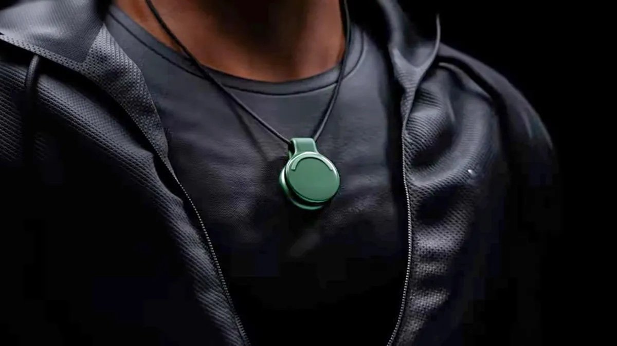 Person wearing a black shirt and jacket with a round, green pendant on a black cord necklace.