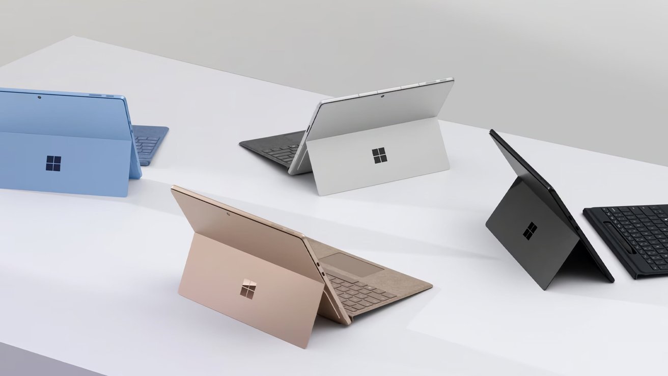 Five laptops in blue, silver, grey, black, and bronze colors, arranged on a white surface with their kickstands open.