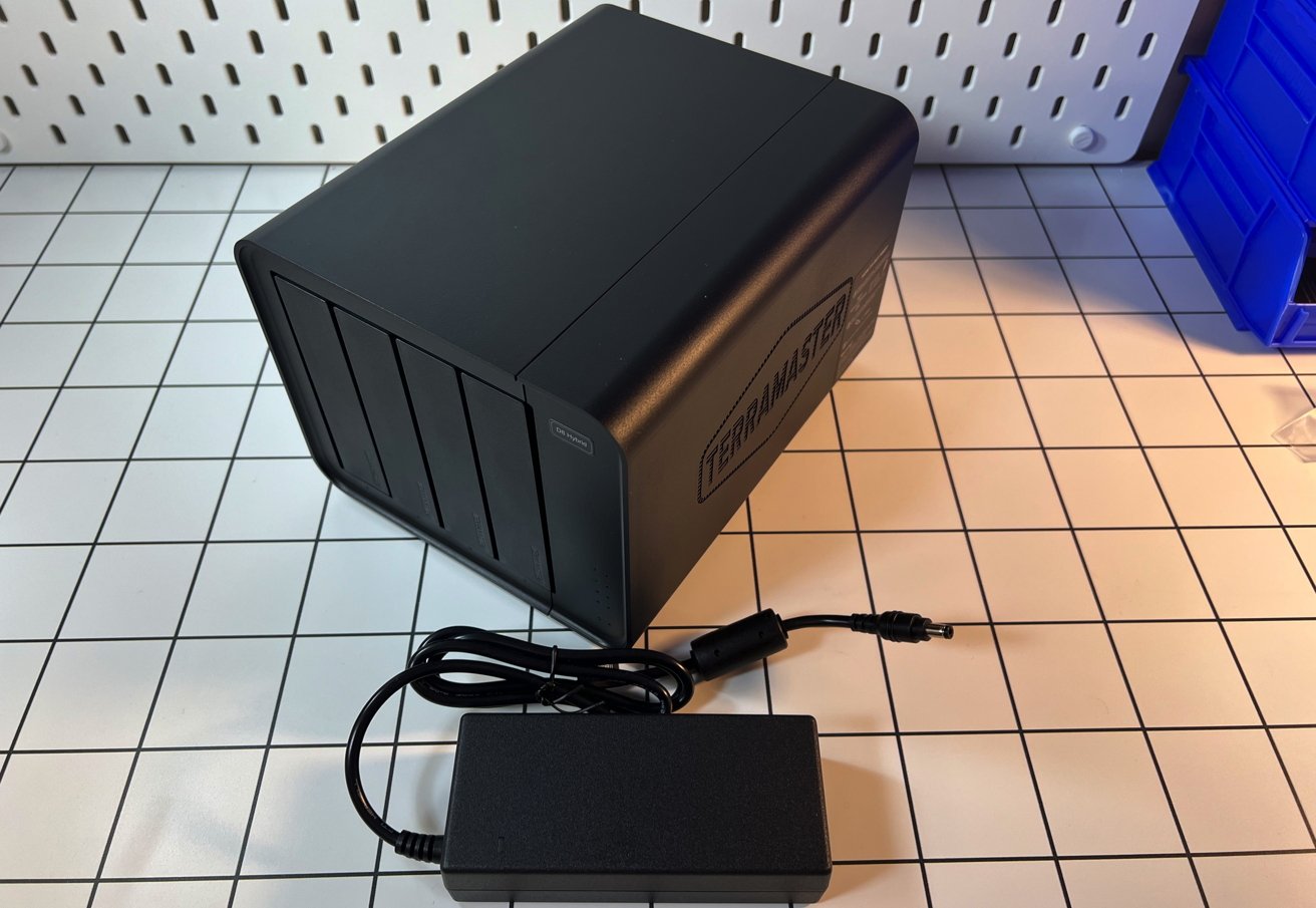Black TerraMasterD8 Hybrid device with multiple drive bays, sitting on a white grid-patterned surface. A black power adapter and cord are placed in front of it.