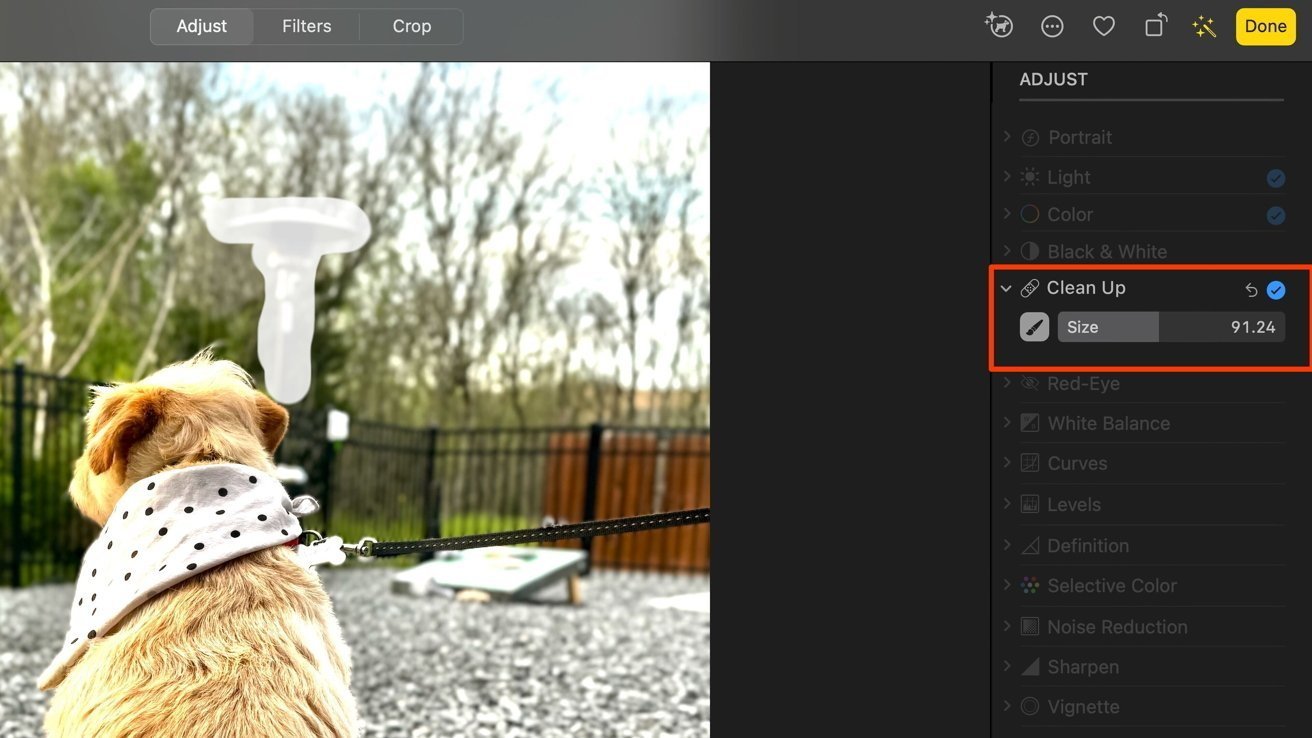 Small dog with a white polka dot bandana sitting outside, facing away; trees and a fence in the background, photo-editing options visible on the right.