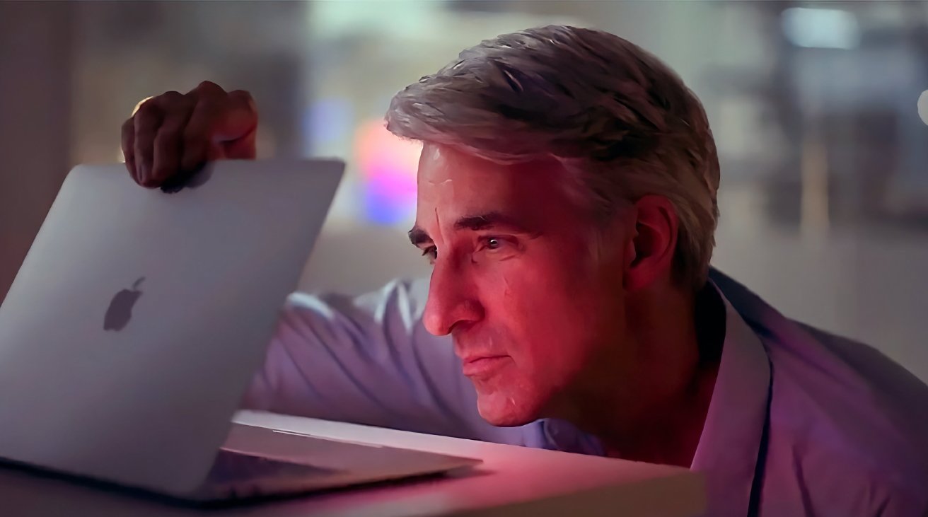 Man with gray hair, wearing a light shirt, closely inspecting an open laptop illuminated by a soft pink light.