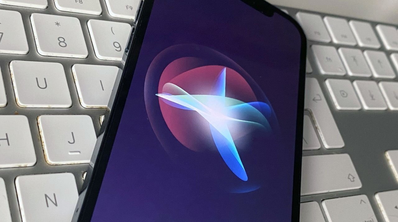 iPhone with a colorful Siri animation is laying on a white computer keyboard.