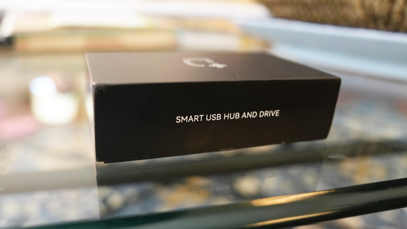 Dockcase packaging on a glass table labeled 'SMART USB HUB AND DRIVE' in white text. Blurred background.