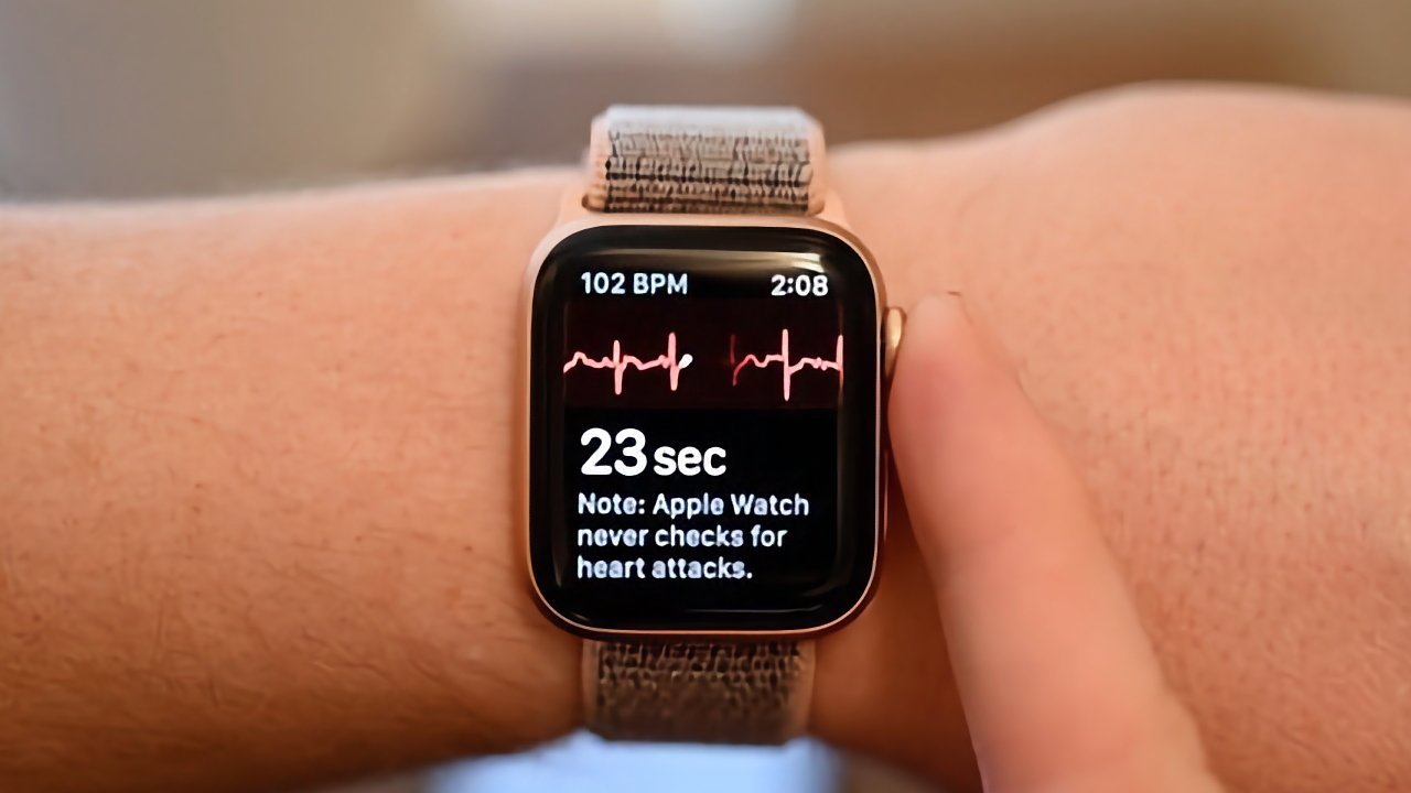 An Apple Watch on the wrist displaying heart rate of 102 BPM, an EKG graph, elapsed time of 23 seconds, and note about heart attack detection limitations.
