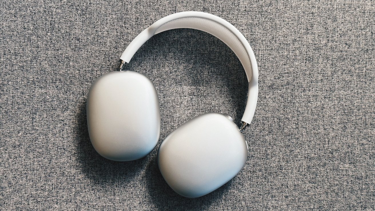 White over-ear headphones with cushioned ear pads and a padded headband, lying on a textured gray surface.