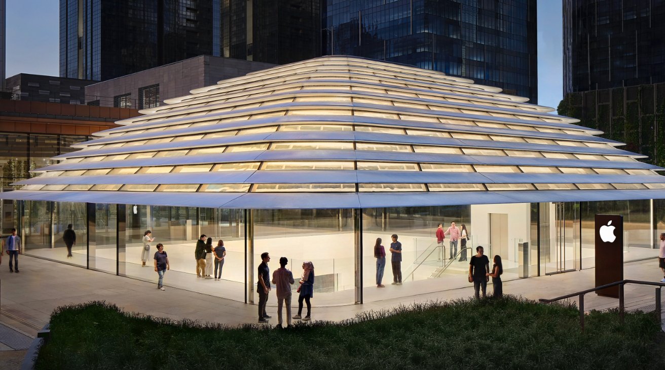A modern glass-walled storefront with a domed roof, featuring an Apple logo, surrounded by people conversing outside, with a cityscape background.