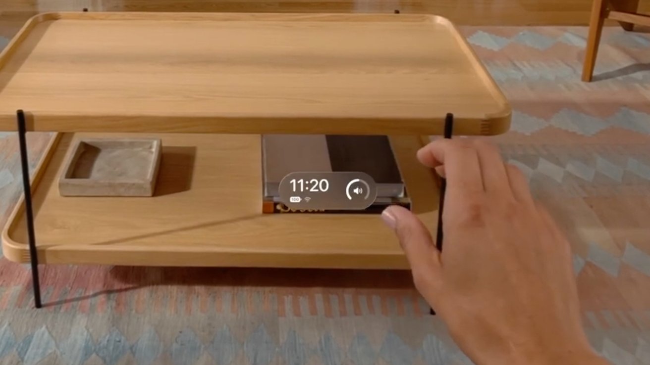 A hand reaching out, palm down, with the new Control Center widget hovering above it displaying the time, battery, and Wi-Fi in a modern room with a wooden table