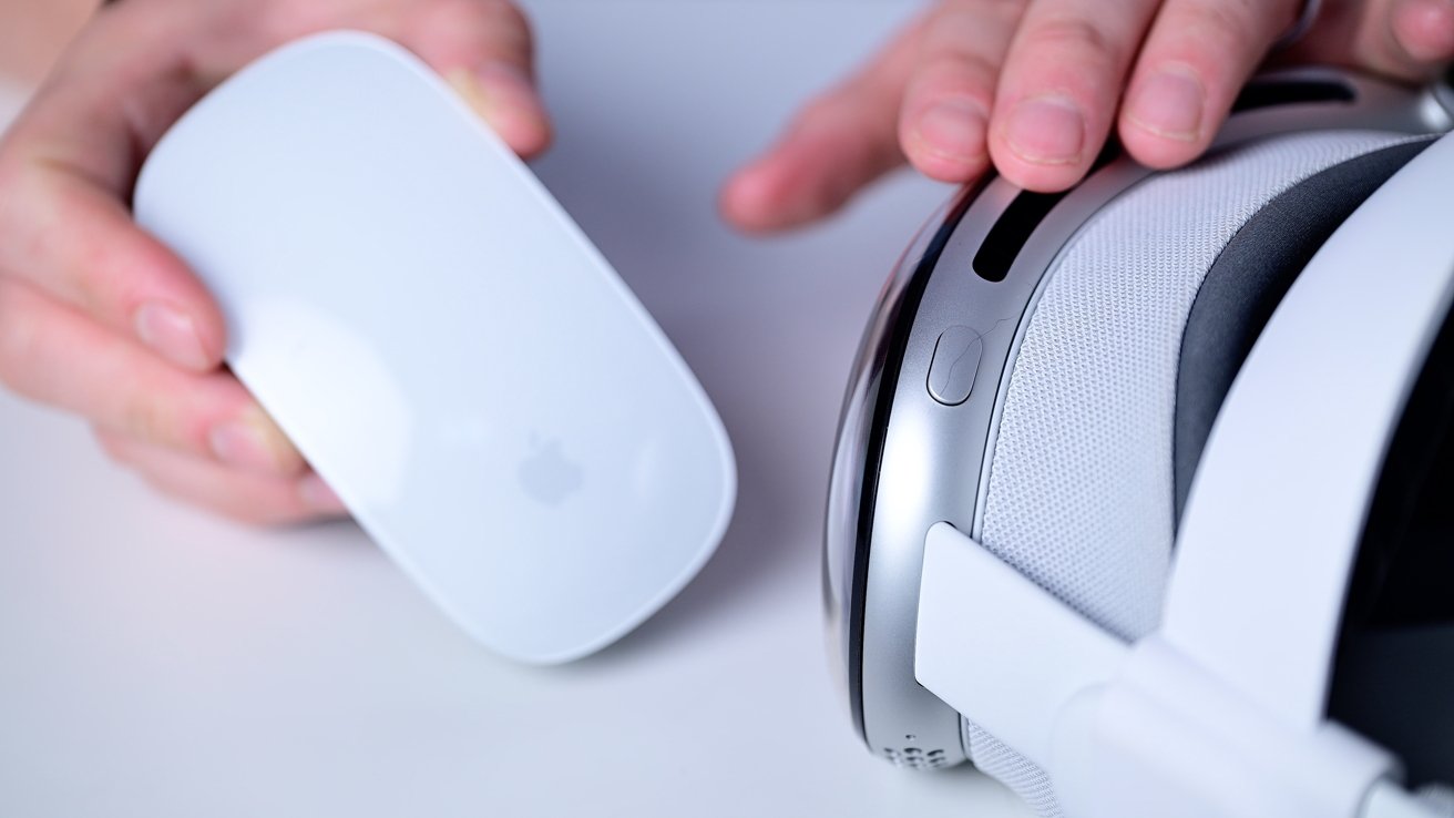Hands holding a white computer mouse and an Apple Vision Pro on a white surface