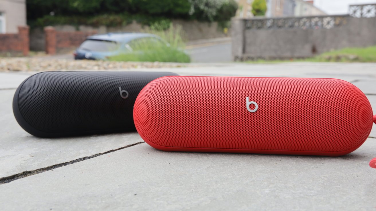 Red and black cylindrical speakers on a concrete surface in an outdoor setting.