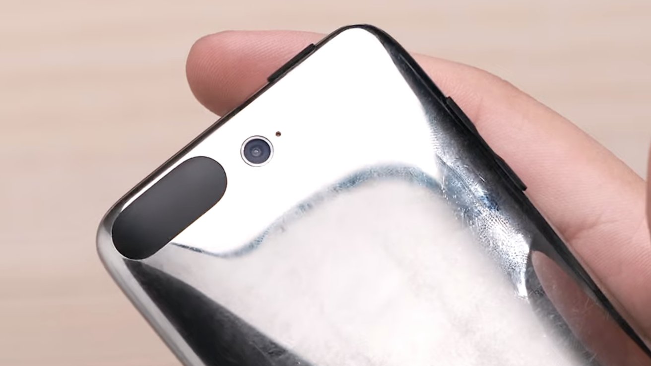 Close-up of a person holding a shiny, reflective phone with a single rear camera and flash.