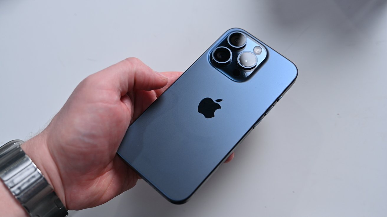 A hand holding a blue smartphone with three rear camera lenses and an Apple logo on its back.