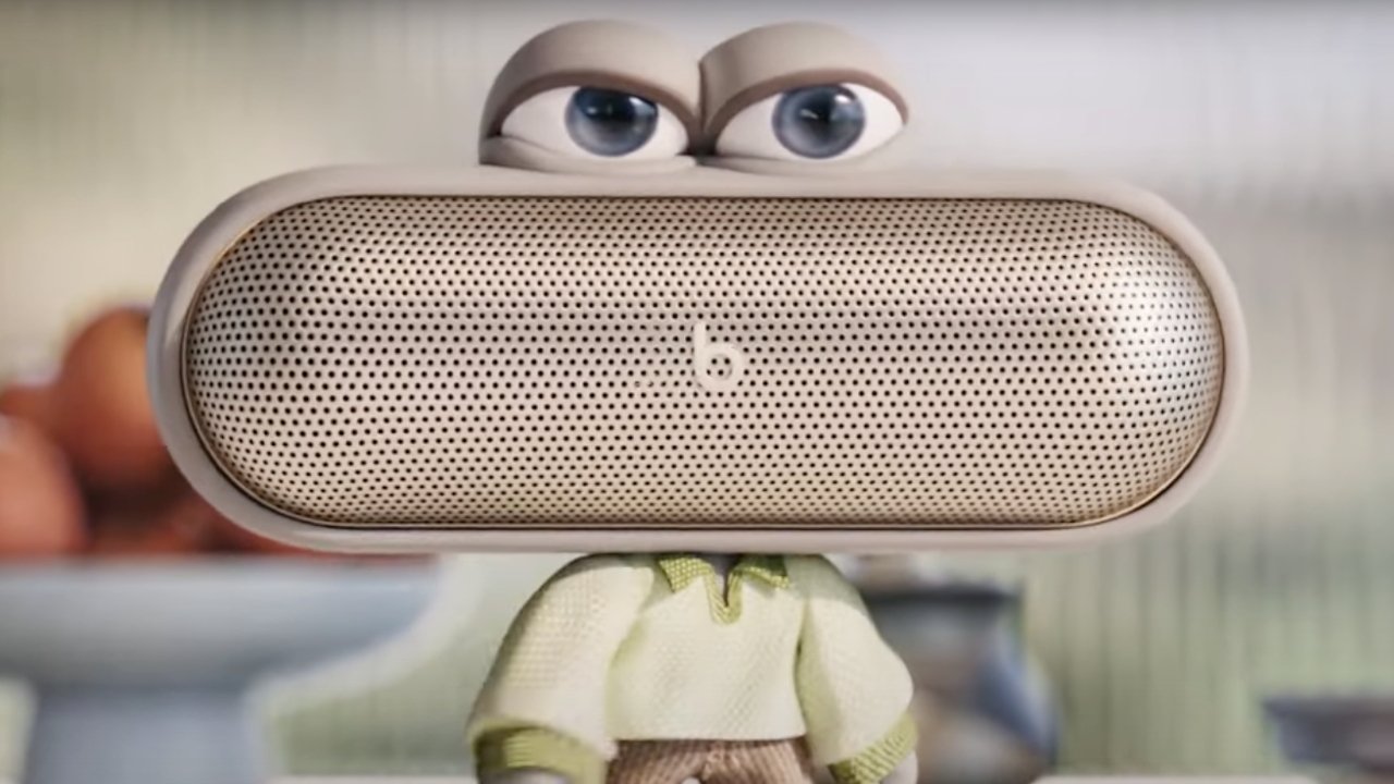 Cartoon Beats Pill+ speaker with large expressive eyes, human-like torso, and arms, set in a kitchen background with a blurred bowl and fruit.