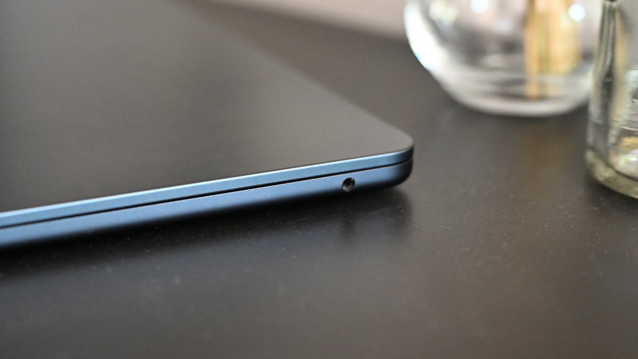 Side view of a closed laptop on a dark surface, with glass objects in the background.