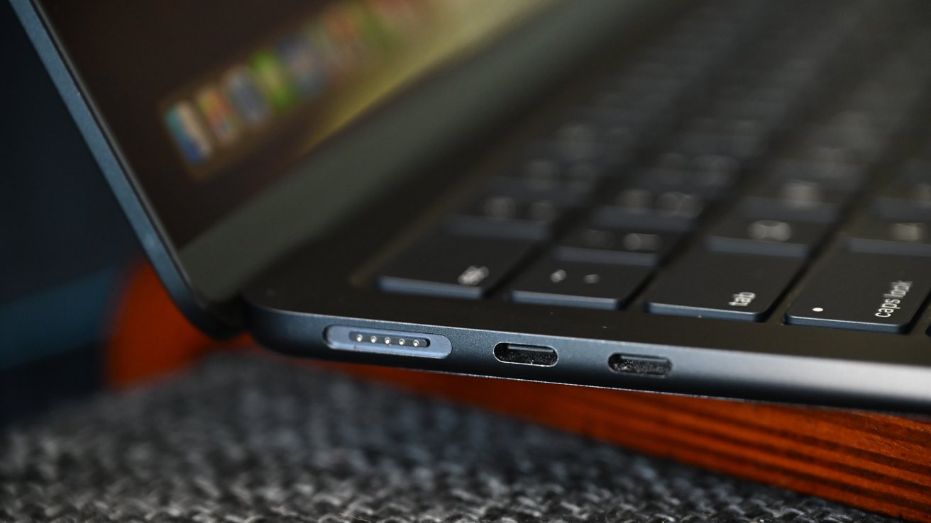 Close-up of a laptop keyboard and ports, including a MagSafe connector and USB-C port, on a textured surface.