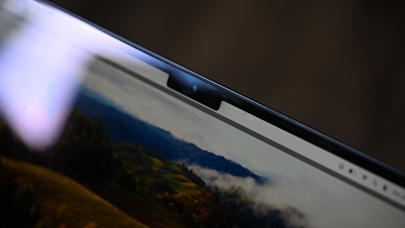 A close-up of a laptop screen's top edge, showing a webcam notch and a countryside landscape on the display.