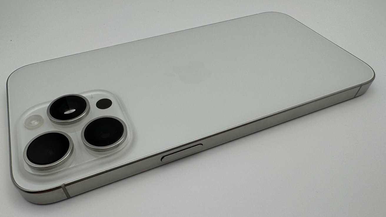 A silver smartphone with three camera lenses on the back lies on a white surface.