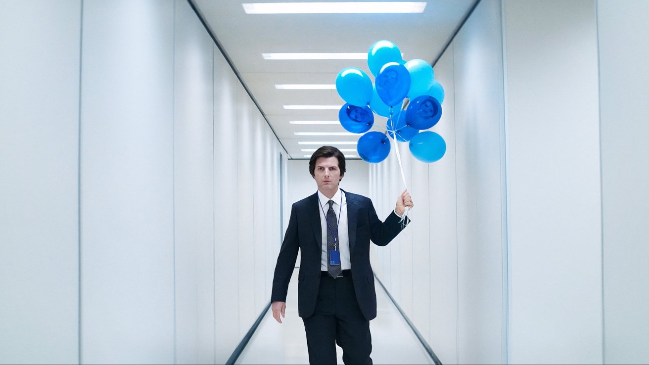 Man in a suit holding blue balloons while walking down a brightly lit, white hallway with a stern expression.