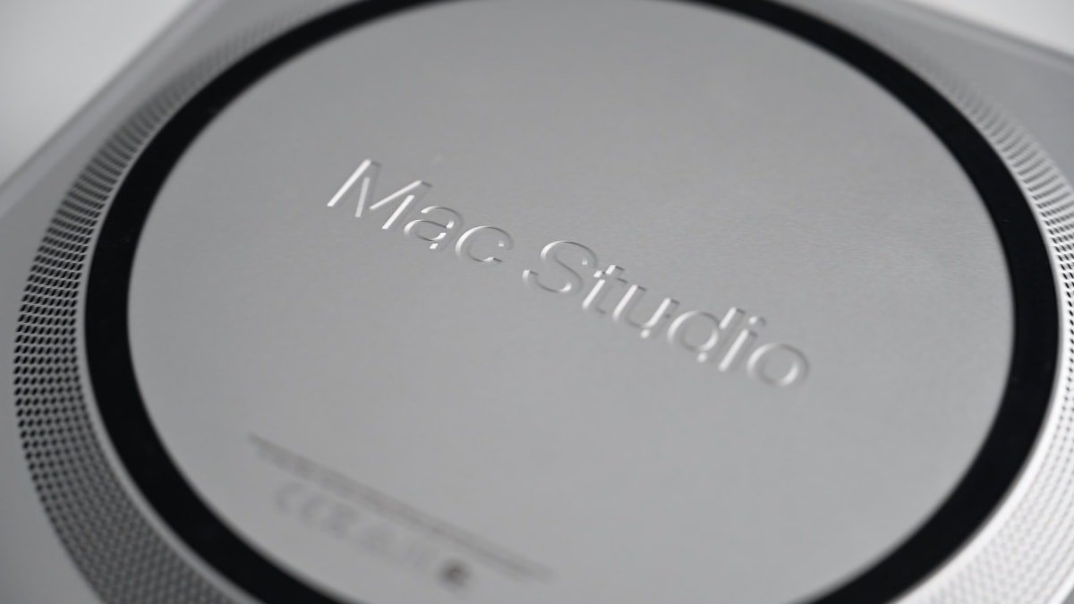 Close-up of a circular Mac Studio label on a metallic surface, displaying embossed text within a black ring.