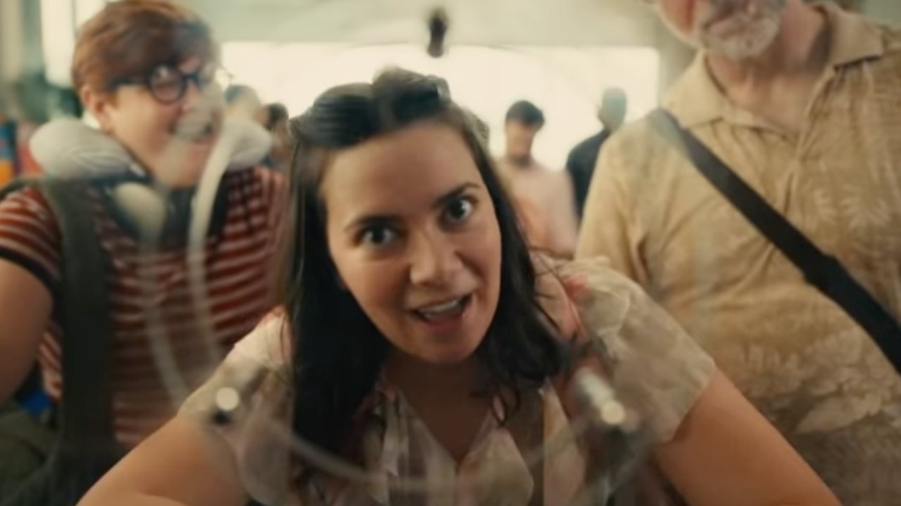 Woman with a curious expression leans toward the camera, with two people smiling in the background at a busy place.