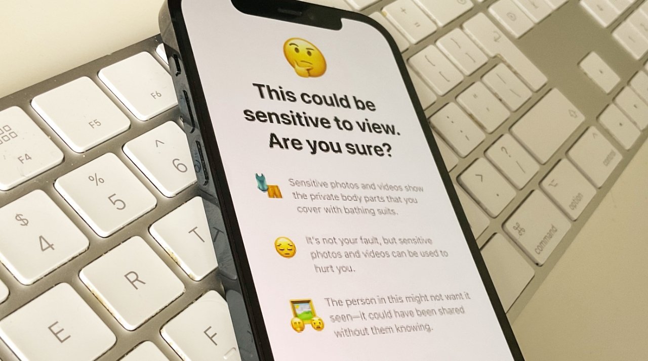 Smartphone displaying a sensitive content warning, laid on a white keyboard.