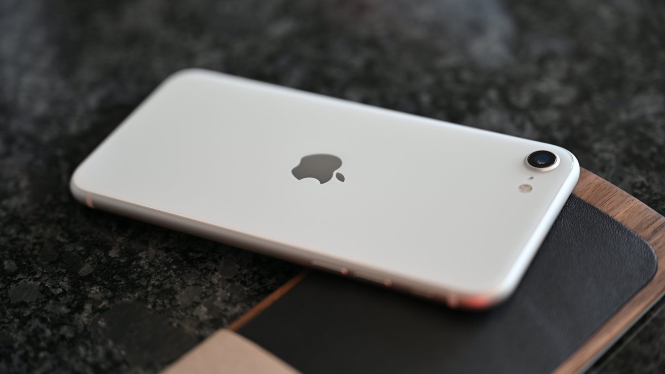 White smartphone with a single rear camera and an apple logo, resting on a dark surface.