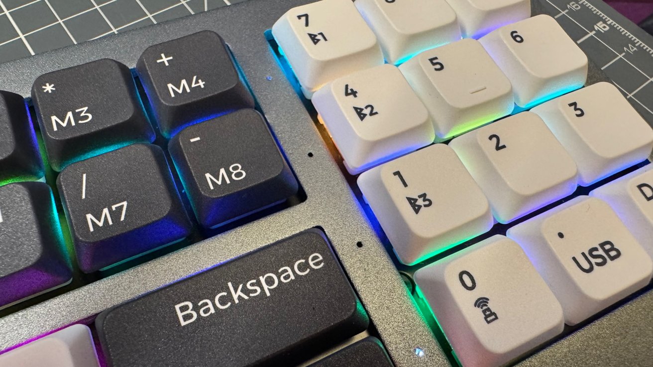 Close-up of a mechanical keyboard with black and white keys labeled M3 to M8, numbers, and symbols, featuring backlighting in various colors.