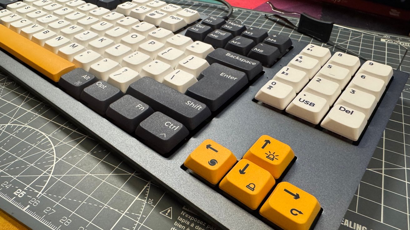 Mechanical keyboard with gray, white, and yellow keycaps on a cutting mat background.