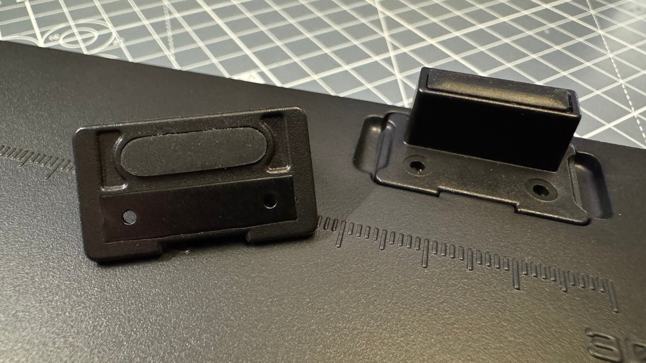 Two black plastic clips on a black surface with embossed measurement markings, set on a grid-patterned cutting mat background.