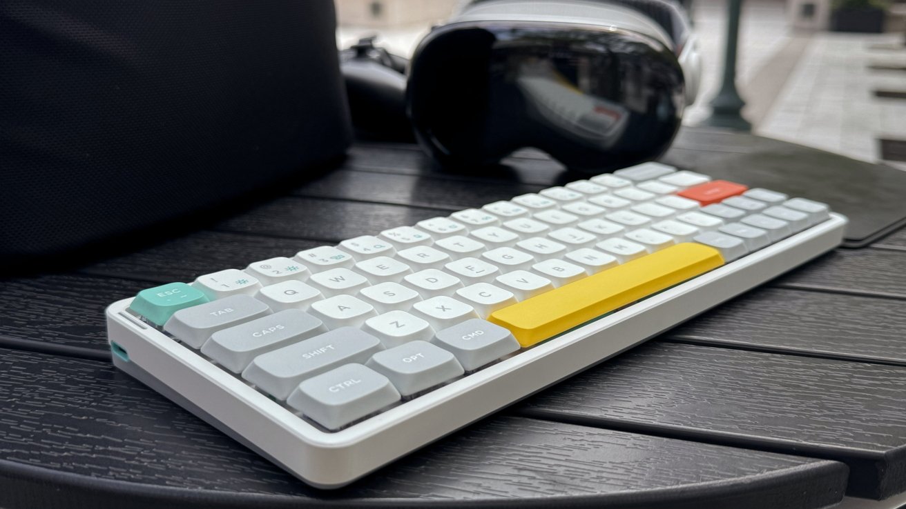 Nuphy Air60 keyboard with colorful keys on a round, wood-patterned table next to Apple Vision Pro