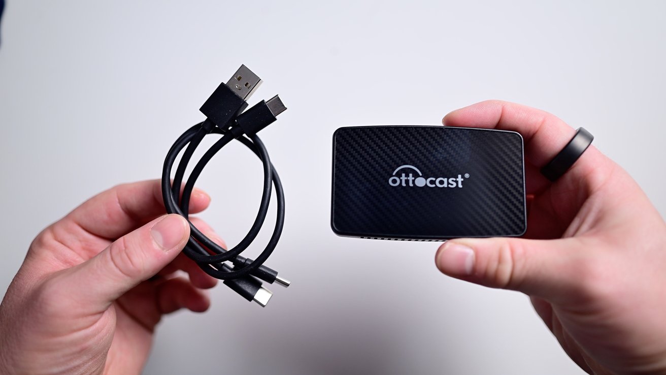 Hands holding a coiled USB cable and a small black rectangular device with the word 'Ottocast' on it.