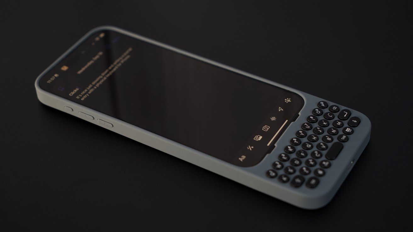 Smartphone with a physical QWERTY keyboard attachment, placed on a dark surface, displaying a text message on the screen.