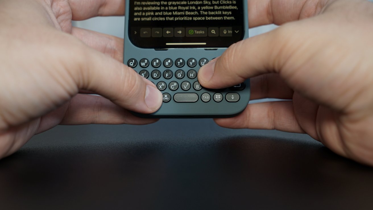 Hands typing on a small physical keyboard attached to a mobile device with a screen displaying text.