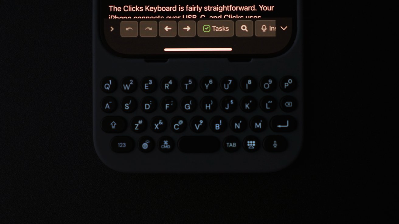 A close-up of a physical keyboard with backlit circular keys connected to a smartphone displaying text.