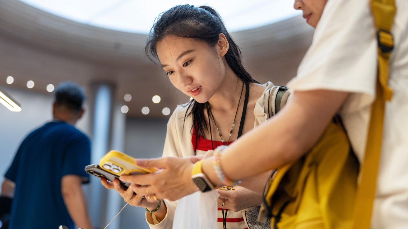 Woman attentively looking at a smartphone with another person in a brightly lit, indoor setting.