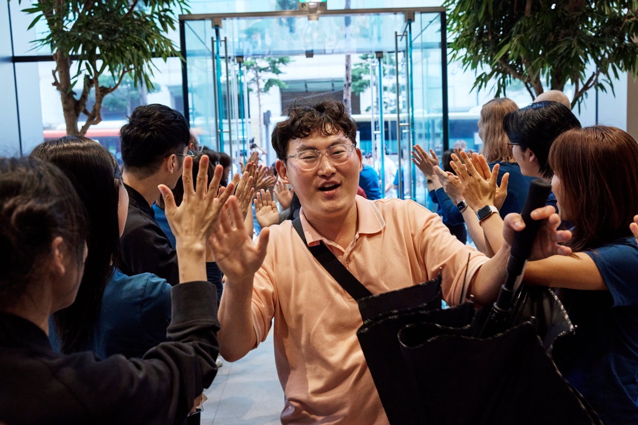 A man in a pink shirt walks through a line of people giving high fives.