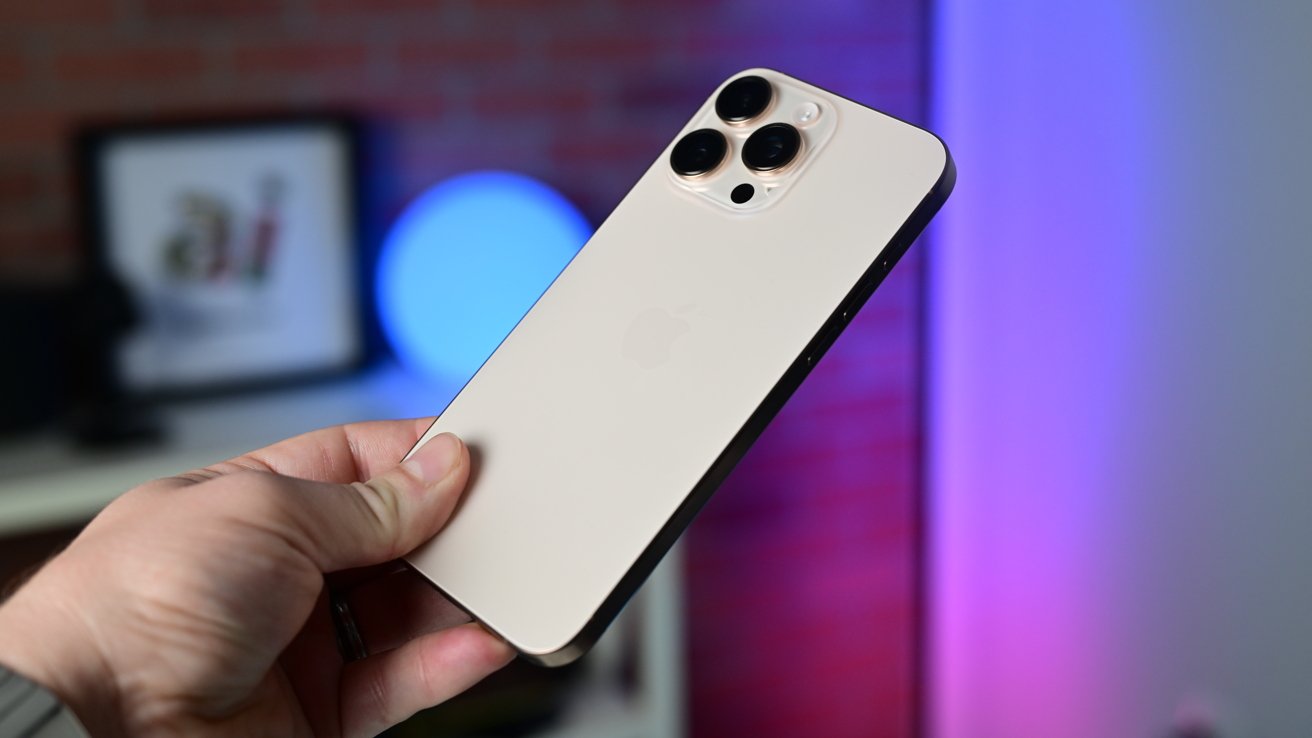 The desert titanium iPhone 16 Pro Max behind held in bright studio light