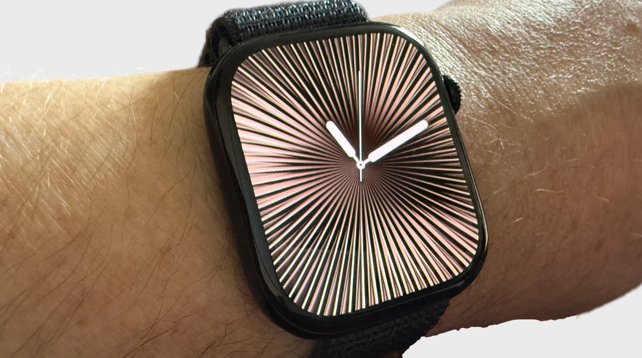 A wrist wearing a smartwatch with a black band and a watch face displaying a radial pattern with white clock hands.