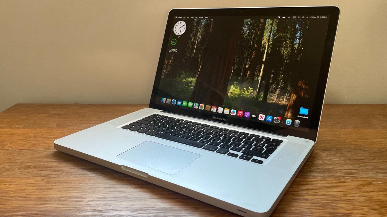 Laptop on a wooden desk displaying a forest wallpaper and various app icons on the screen, including a clock and battery status at 96%.