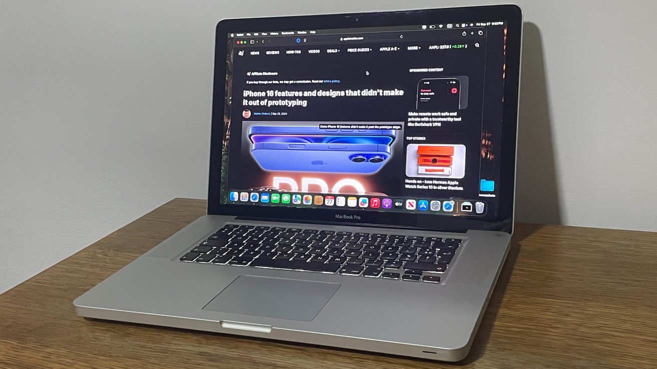 Open MacBook Pro on a wooden desk displaying a tech news website about iPhone 16 features and design.